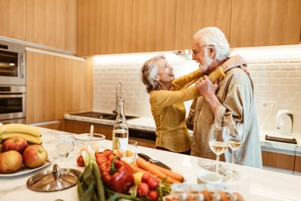 Two seniors embrace and smile as they stand in the kitchen of their luxury senior apartment.
